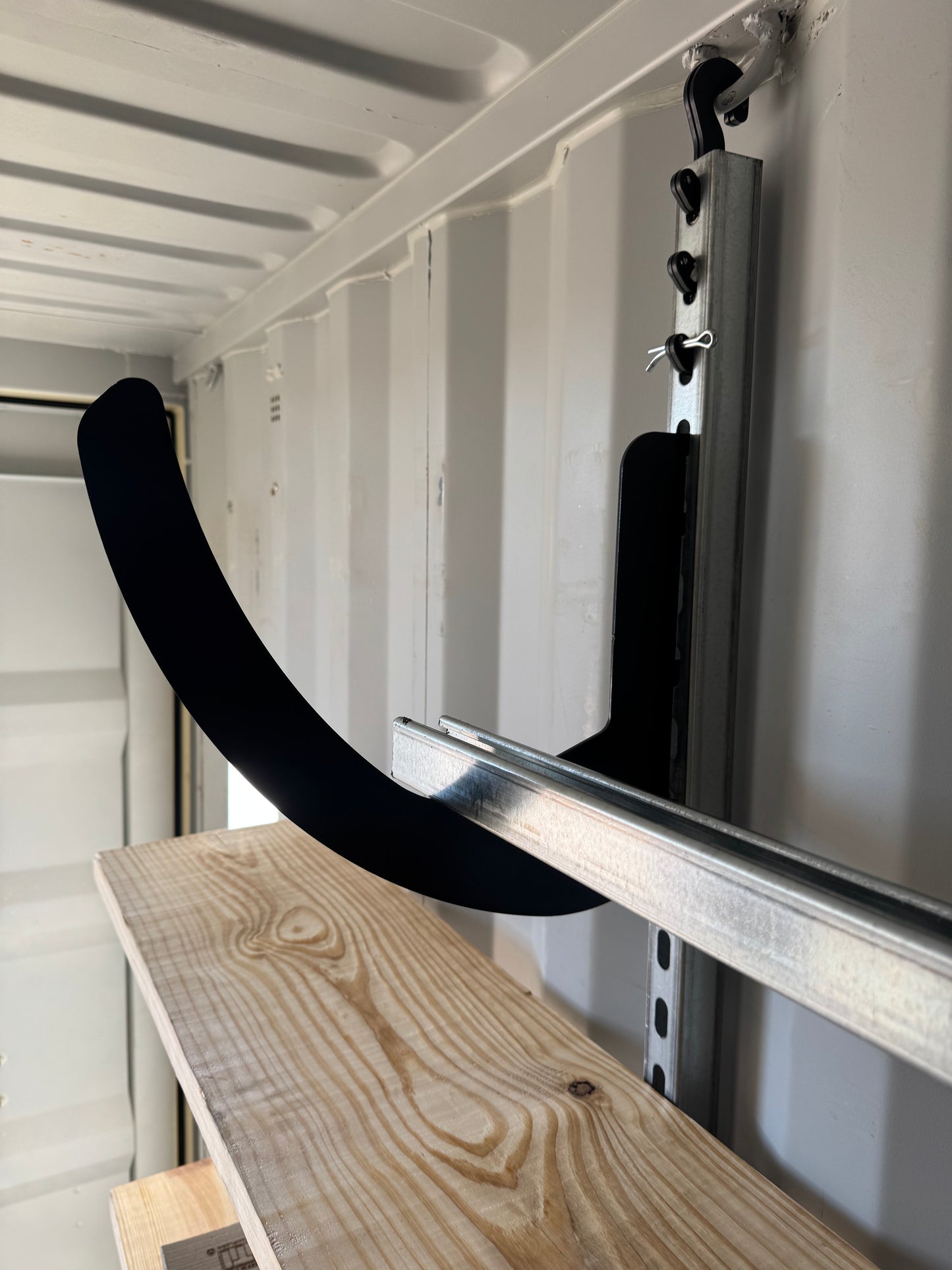 Mounted metal rail with a curved bracket holding a wooden shelf inside a storage container.