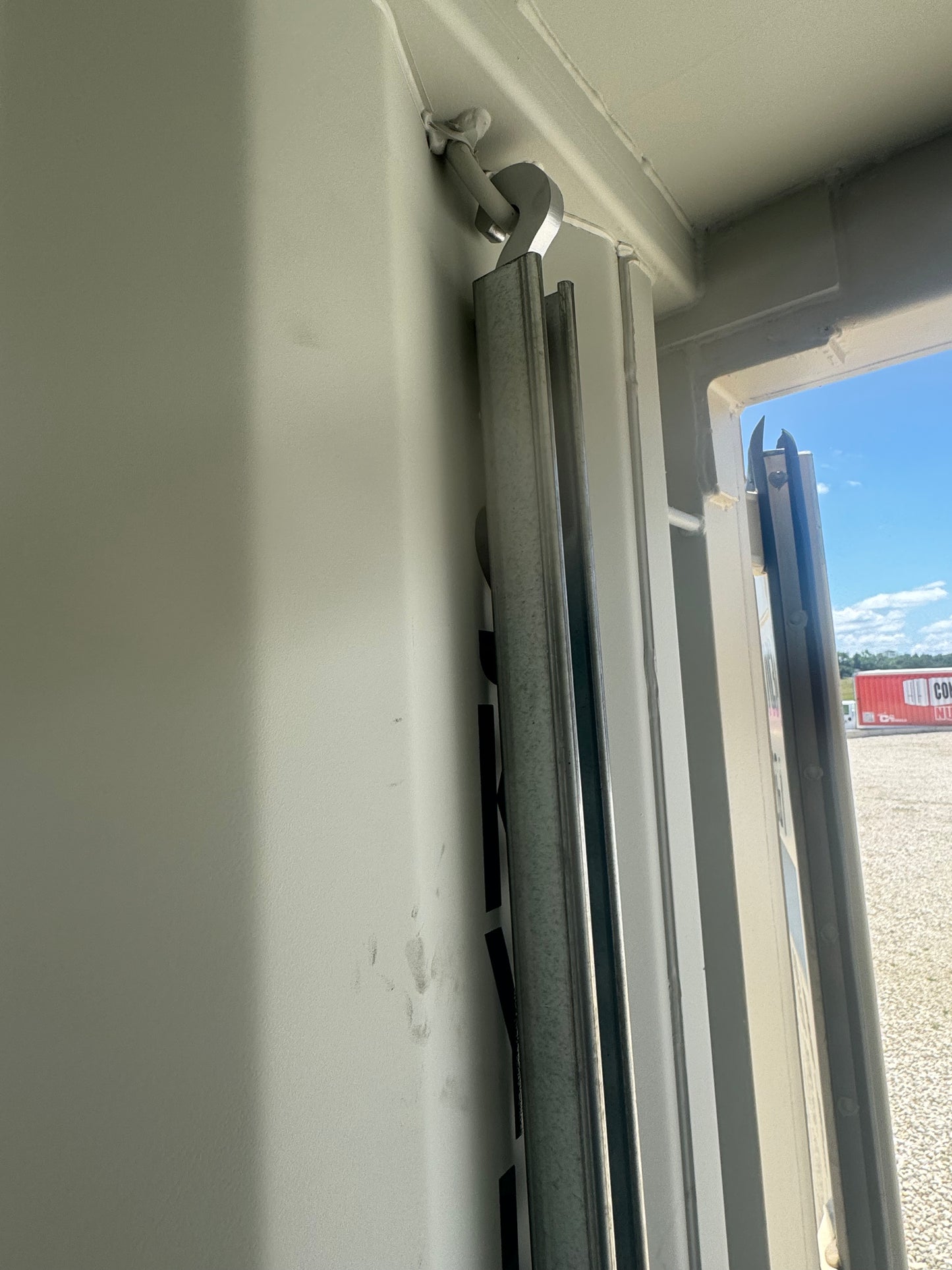 Top-mounted metal hanger attached to a vertical strut channel near the open container door.