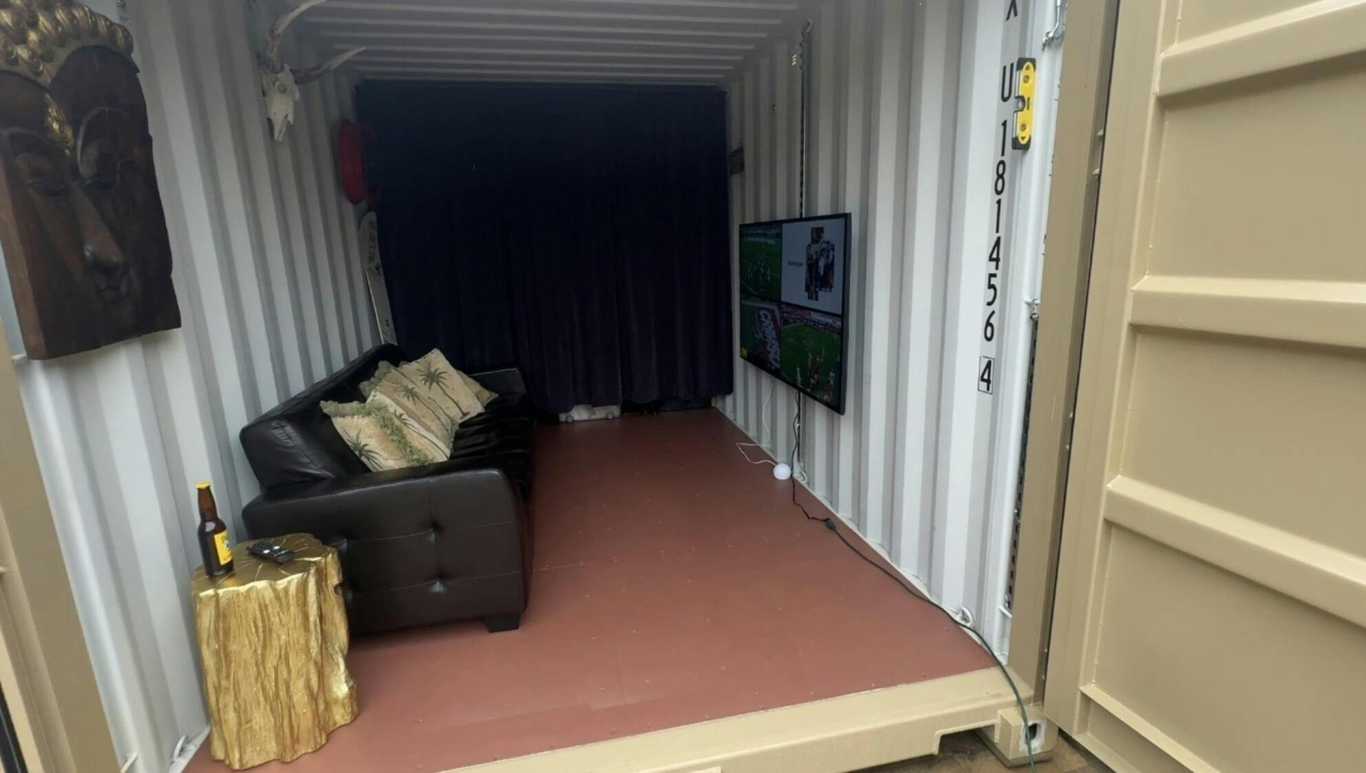 Shipping container lounge with sofa and wall-mounted TV against dark curtains